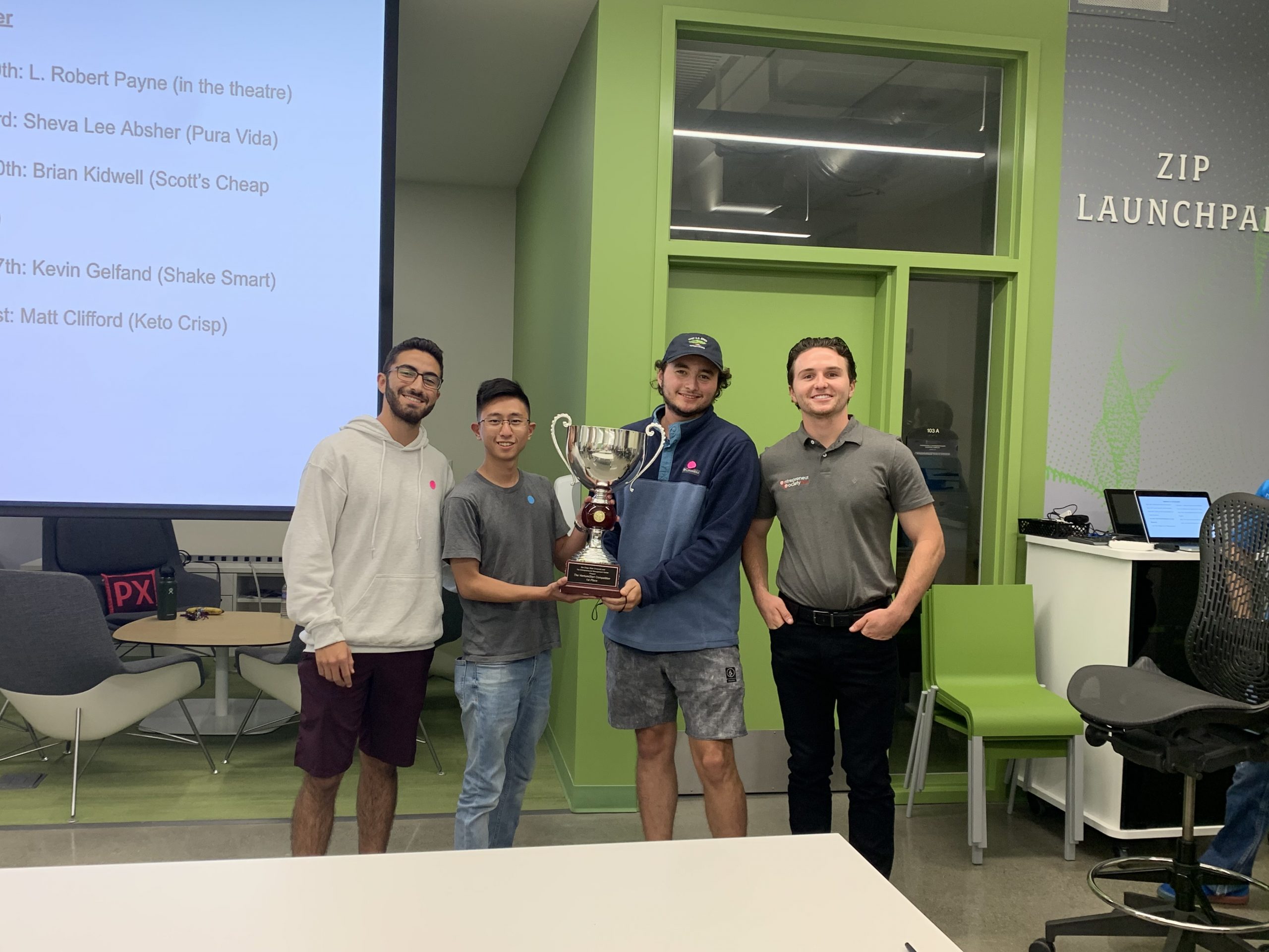 Four male students celebrate winning the competition. Jason Sunardi (second from left) and Conor Phan hold the trophy