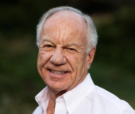 A man in a white shirt smiles outside