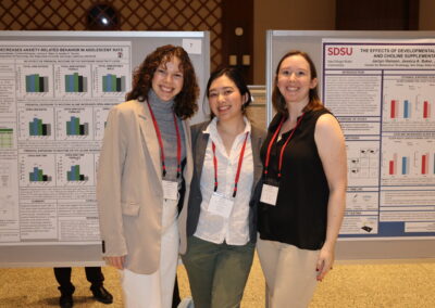Three students stand smiling in front of their posters on psychology research