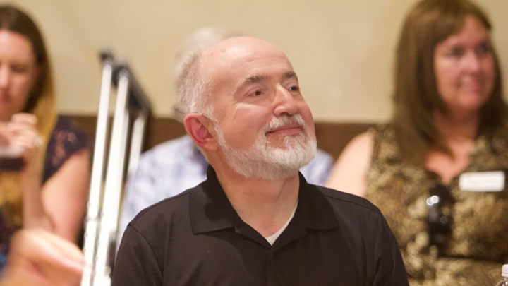 Paul Paolini sitting within small crowd indoors.